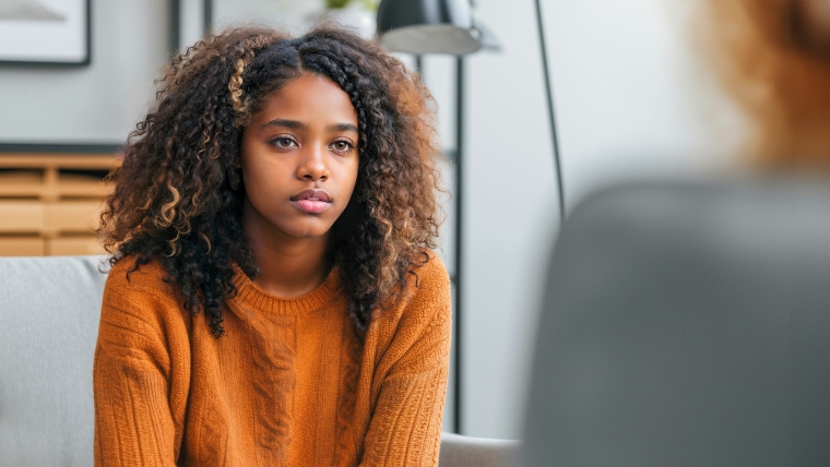 How a Psychiatrist Helps Identify and Treat Teen Depression Teen girl sitting on a couch in a psychiatrist office looking sad and serious | How a Psychiatrist Helps Identify and Treat Adolescent Depression | Mindful Health Solutions