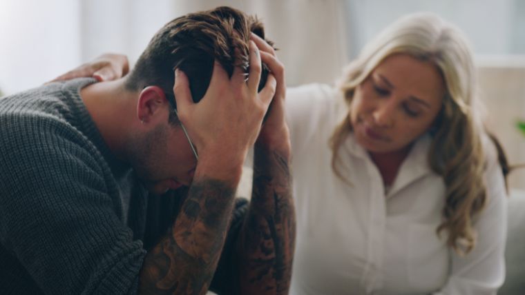 How To Help Someone Calm an Anxiety Attack A man with his head in his hands being supported by a woman | How To Help Someone Calm an Anxiety Attack