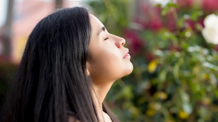 Master-Stress-and-Anxiety-Deep-Breathing-Techniques-for-Better-Mental-Health Woman with eye closed, deep breathing, with flowers in the background | Master Stress and Anxiety Deep Breathing Techniques for Better Mental Health | Mindful Health Solutions