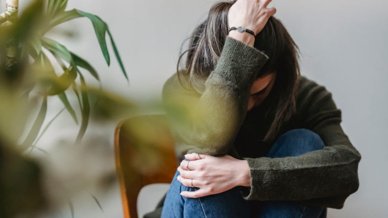 Feminine person curled up into herself, with an arm around her leg and a hand in her hair | A Deep Dive into the 8 Distinct Types of Anxiety | Mindful Health Solutions