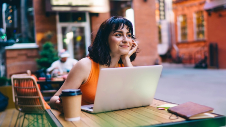 Balancing-Work-Life-and-TMS-Therapy-Tips-for-Success Female person working outside at a cafe, smiling with her head in her hand | Balancing Work, Life, and TMS Therapy Tips for Success | Mindful Health Solutions