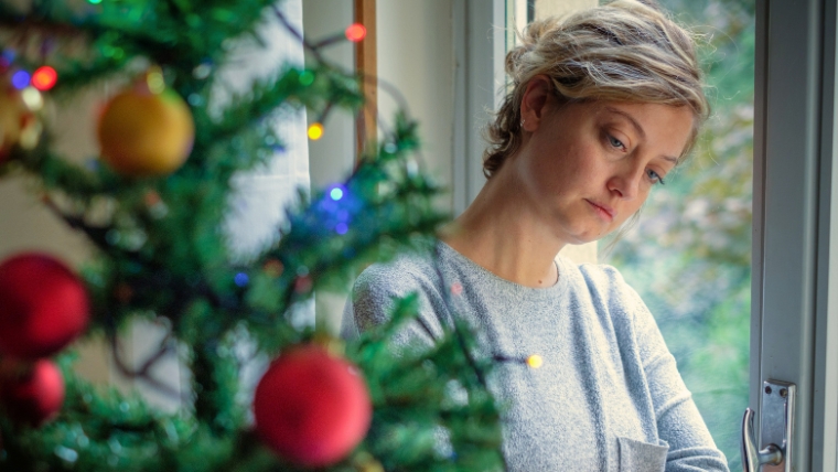 Transform-Your-Holidays-10-Proven-Techniques-to-Manage-Depression Woman leaning on window, looking sad and distant, with a Christmas tree in the foreground | Transform Your Holidays 10 Proven Techniques to Manage Depression | Mindful Health Solutions