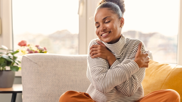 Start the New Year Right with a Quick Mental Health Check-In Woman on couch hugging herself and smiling | Start the New Year Right with a Quick Mental Health Check-In | Mindful Health Solutions