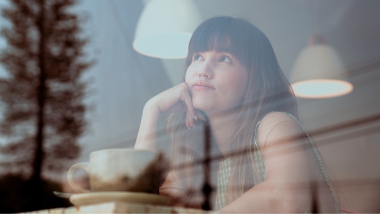 Unlock the Power of Reflection and Set Powerful Mental Health Goals Young woman at a coffee shop looking thoughtfully out a window | Unlock the Power of Reflection and Set Powerful Mental Health Goals | Mindful Health Solutions