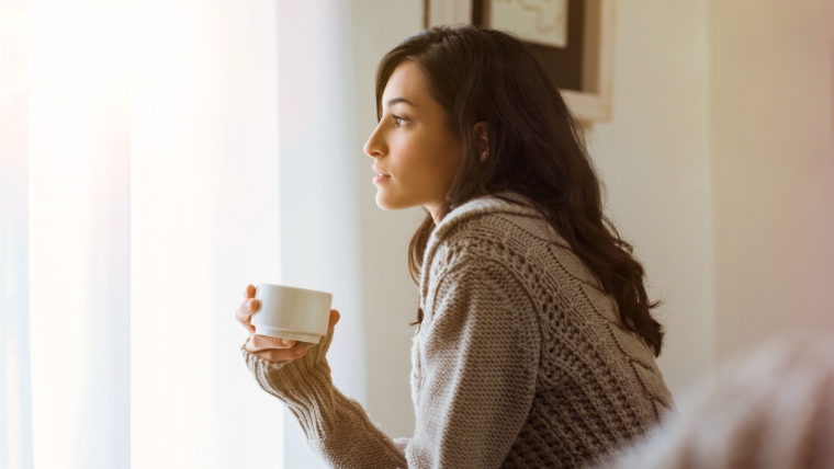 Accelerated-TMS-vs.-Traditional-TMS-Which-One-Makes-Sense-for-You Woman drinking tea on bed thinking seriously | Accelerated TMS vs. Traditional TMS Which One Makes Sense for You | Mindful Health Solutions