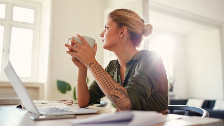 Is-Accelerated-TMS-Safe-5-Potential-Side-Effects-to-Make-Informed-Decisions A person sitting at a table with a laptop and a cup of coffee looking thoughtfully out the window | Is Accelerated TMS Safe 5 Potential Side Effects to Make Informed Decisions | Mindful Health Solutions