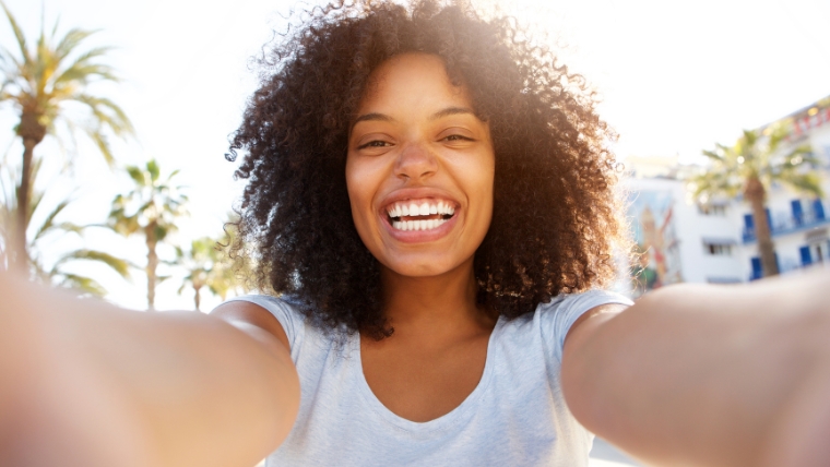 The Speed of Relief How Quickly Does Esketamine Therapy Relieve Depression A woman taking a selfie with a big smile in front of palm trees | How Fast Does Esketamine Relieve Depression Compared to Antidepressants? | Mindful Health Solutions