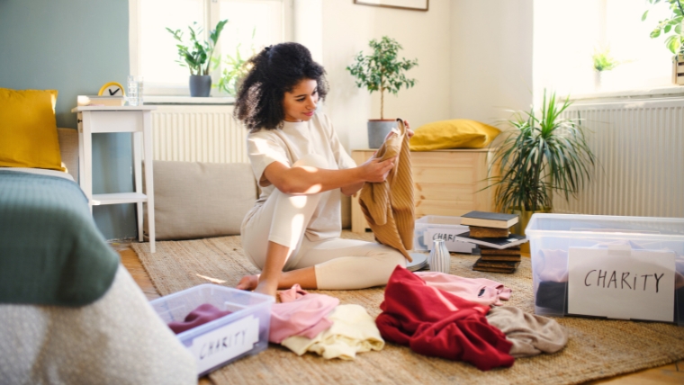 Declutter-Your-Home-Declutter-Your-Mind-The-Path-to-Mental-Clarity A person is sitting on the floor of their bedroom organizing their clothes to see which can be donated to charity | Declutter Your Home, Declutter Your Mind The Path to Mental Clarity | Mindful Health Solutions
