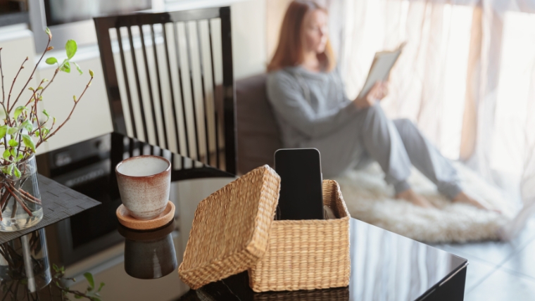 Digital-Detox-How-To-Reclaim-Control-of-Your-Screen-Time-and-Boost-Happiness A phone sitting in a basket while a woman is reading | Digital Detox How To Reclaim Control of Your Screen Time and Boost Happiness | Mindful Health Solutions