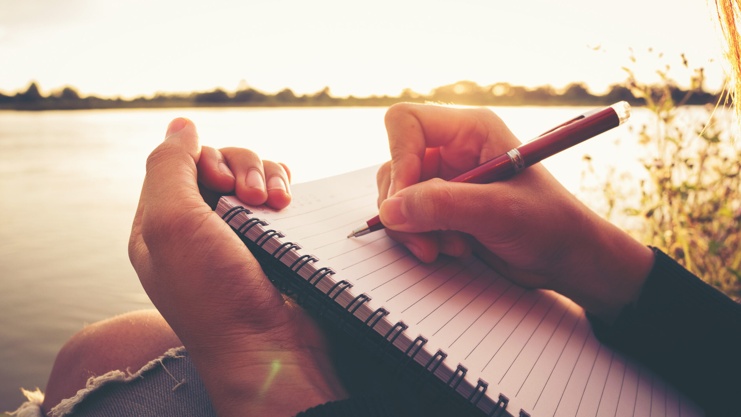 Close up hand of young woman with pen writing on notebook at riv